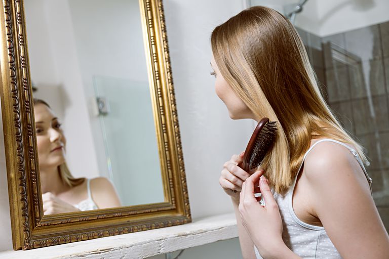 Жена looking in mirror brushing hair